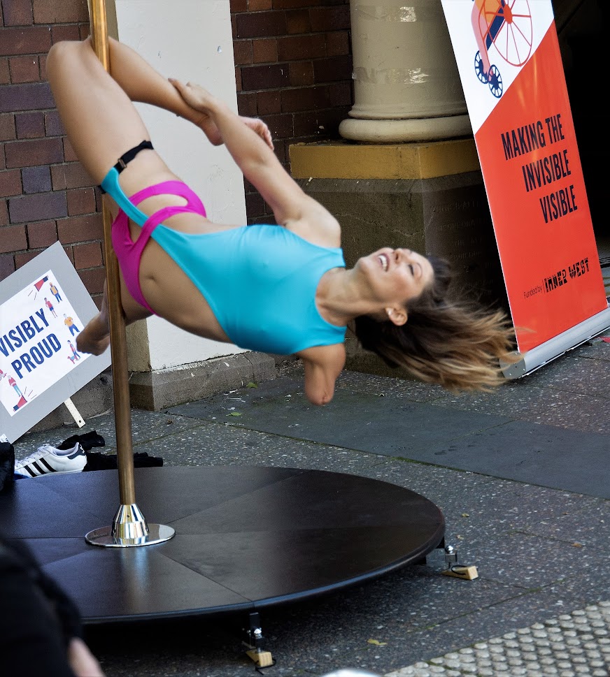A woman with one arm hangs from a pole by one leg 